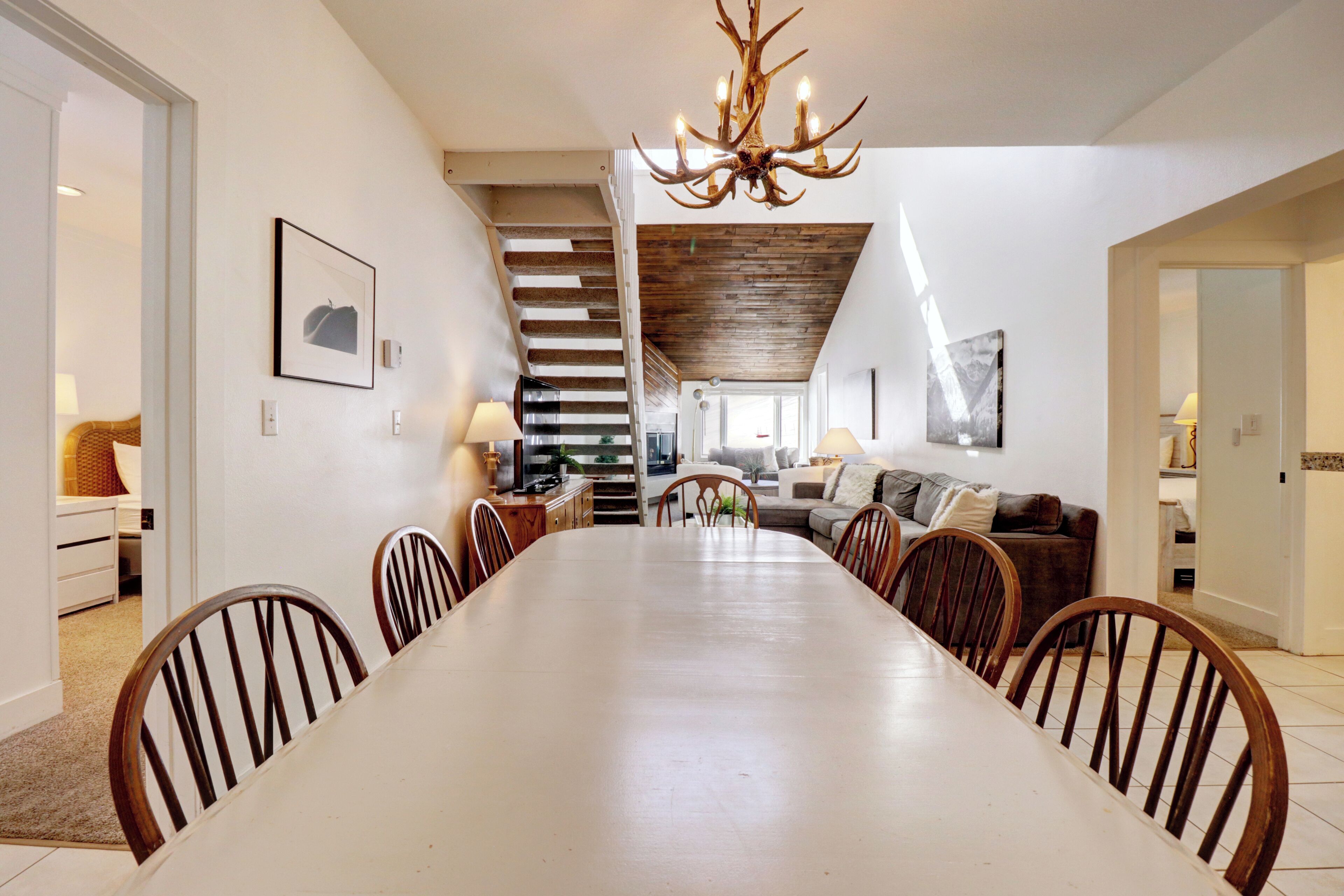 A spacious dining area with a long table and chairs, a chandelier, and a staircase leading to an upper level.