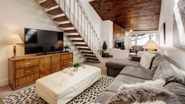 A spacious living room with a high ceiling, a staircase, a flat-screen TV, a sofa, and a coffee table. - Ski In/Out Right By The Lift with Slope side Hot Tub FP304 (Copper Mountain)