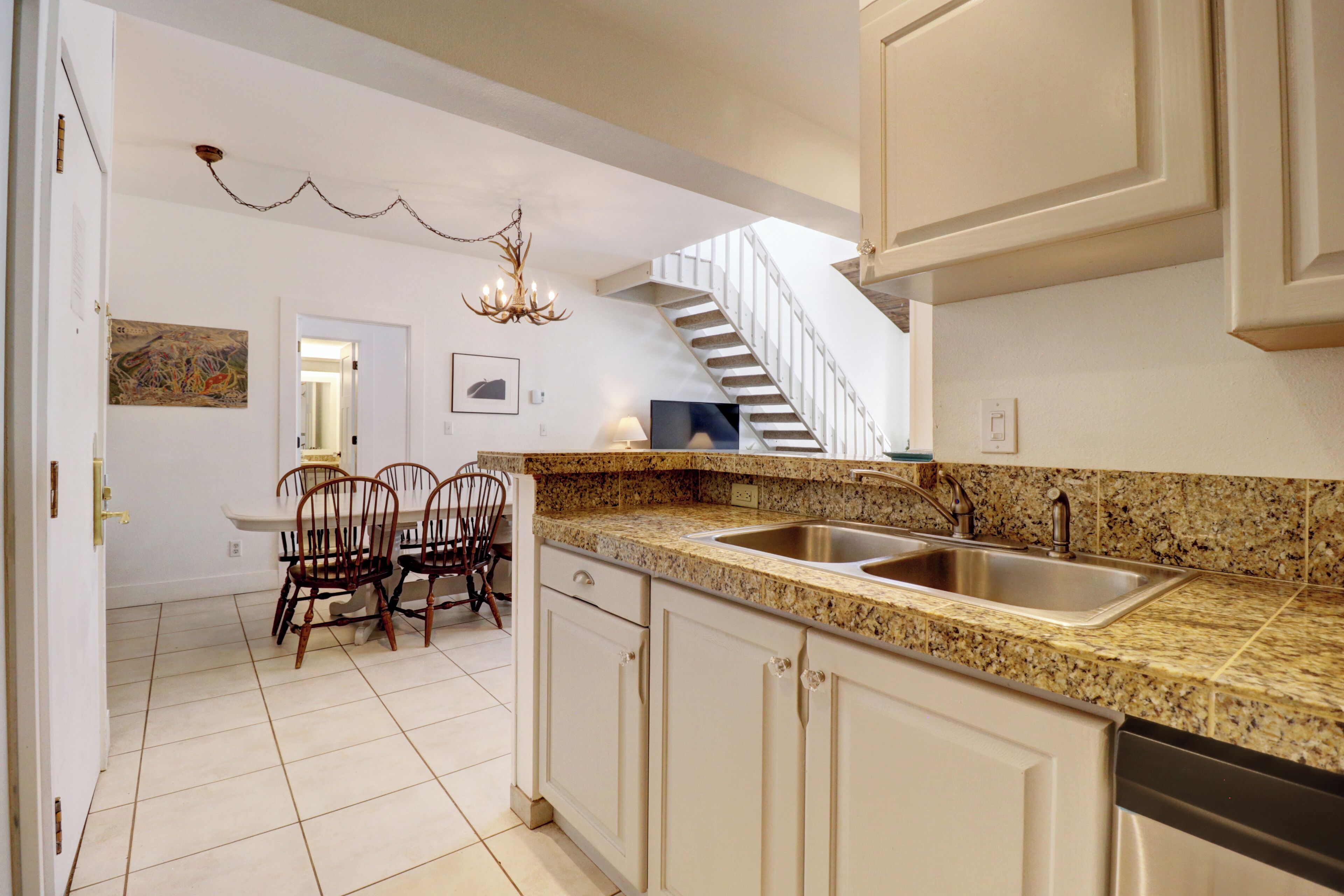 A kitchen with granite countertops, white cabinets, a double sink, and a dining area with chairs and a table.