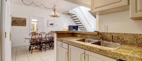 A kitchen with granite countertops, white cabinets, a double sink, and a dining area with chairs and a table.