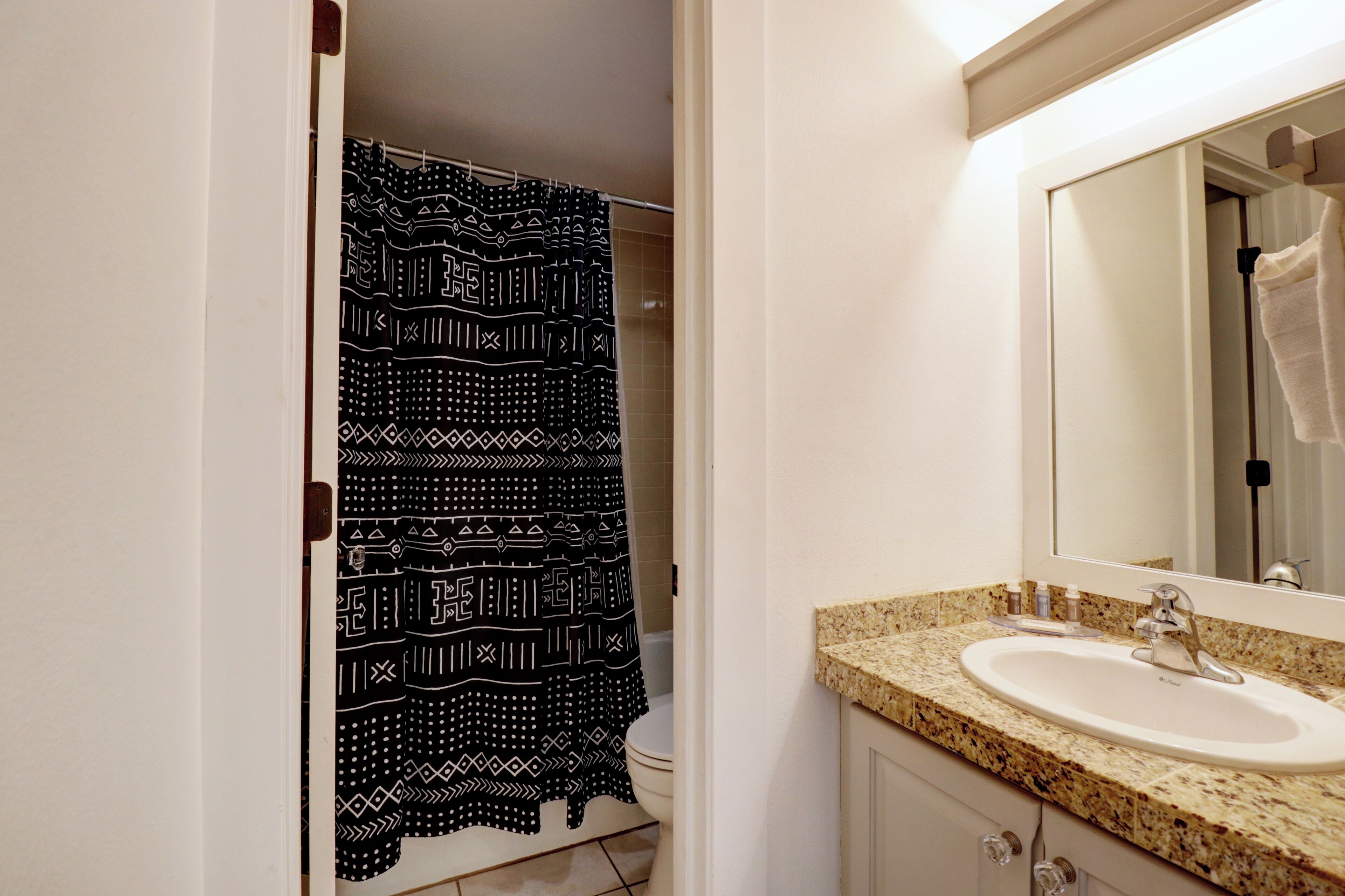 Um banheiro com cortina de chuveiro estampada, pia com espelho e toalha pendurada na parede.