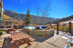 A pool area with a hot tub, wooden deck, and picnic tables.