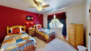 A bedroom with two single beds, a ceiling fan, a window with curtains, a wooden dresser, and a wall painting. - Adventure Villa - 3282, New Private Hot Tub (Moab)