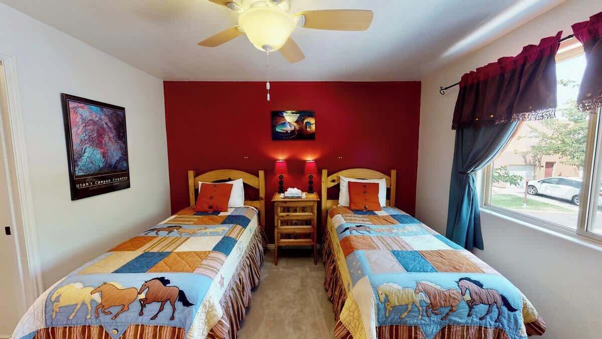 Una habitación con dos camas, un ventilador de techo, un cuadro y una ventana con cortinas.