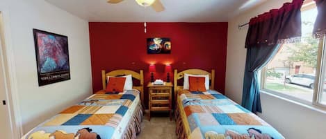 A room with two beds, a ceiling fan, a painting, and a window with curtains.