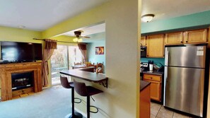 A kitchen with a refrigerator, wooden cabinets, a bar area with stools, and a television. - Adventure Villa - 3282, New Private Hot Tub (Moab)