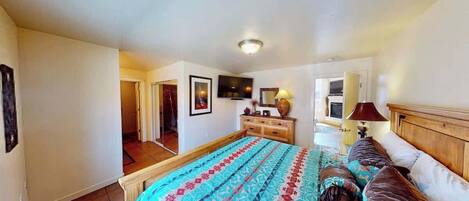 A bedroom with a bed, dresser, television, and a door leading to another room.
