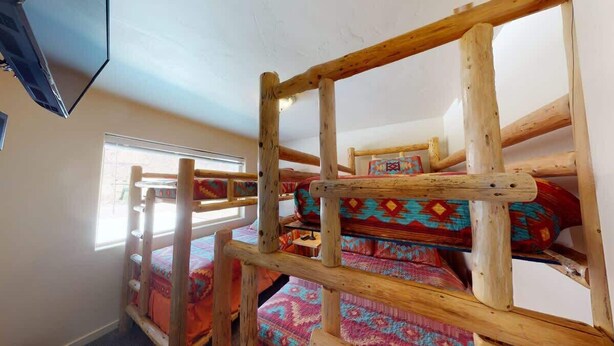 A bunk bed with a wooden frame, a window with blinds, and a colorful bedspread. - Vista Villa - 3A5, Spacious Condo With Panoramic P (Moab)