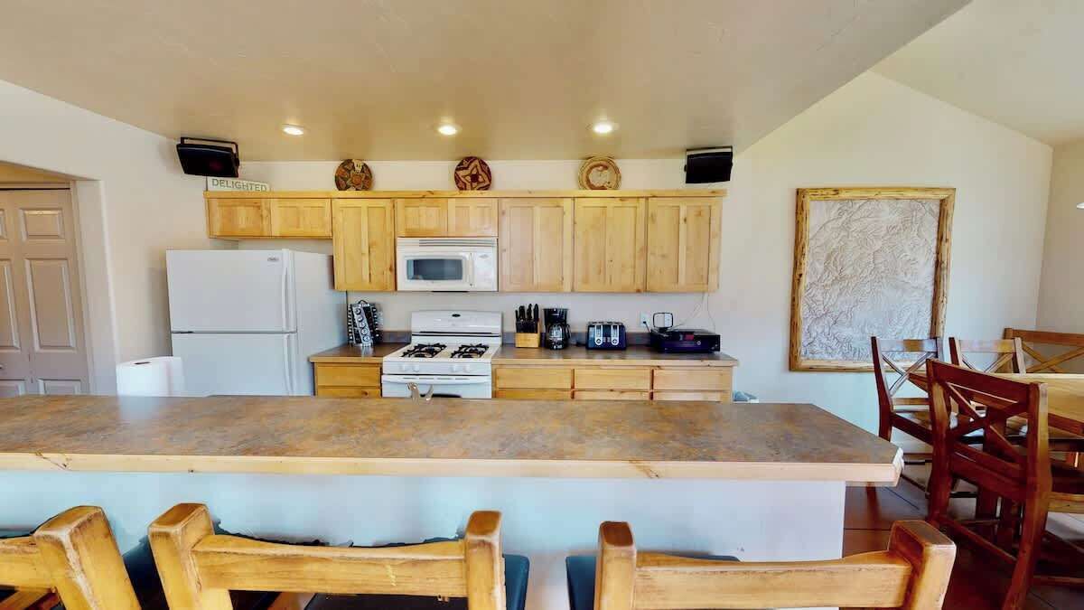 Una cocina con armarios de madera, una isla central y un comedor con sillas de madera.
