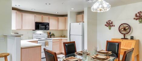 Una cocina moderna con armarios de madera, un refrigerador blanco, un microondas negro y una mesa de comedor de vidrio con sillas.