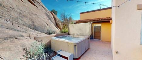 A hot tub in a backyard with a rocky cliff and a building in the background.