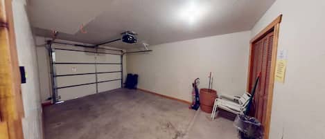 A garage with a ceiling-mounted projector, a closed garage door, and a wooden door with a sign.