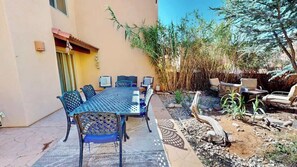 An outdoor patio with a table and chairs, surrounded by plants and a small garden area.