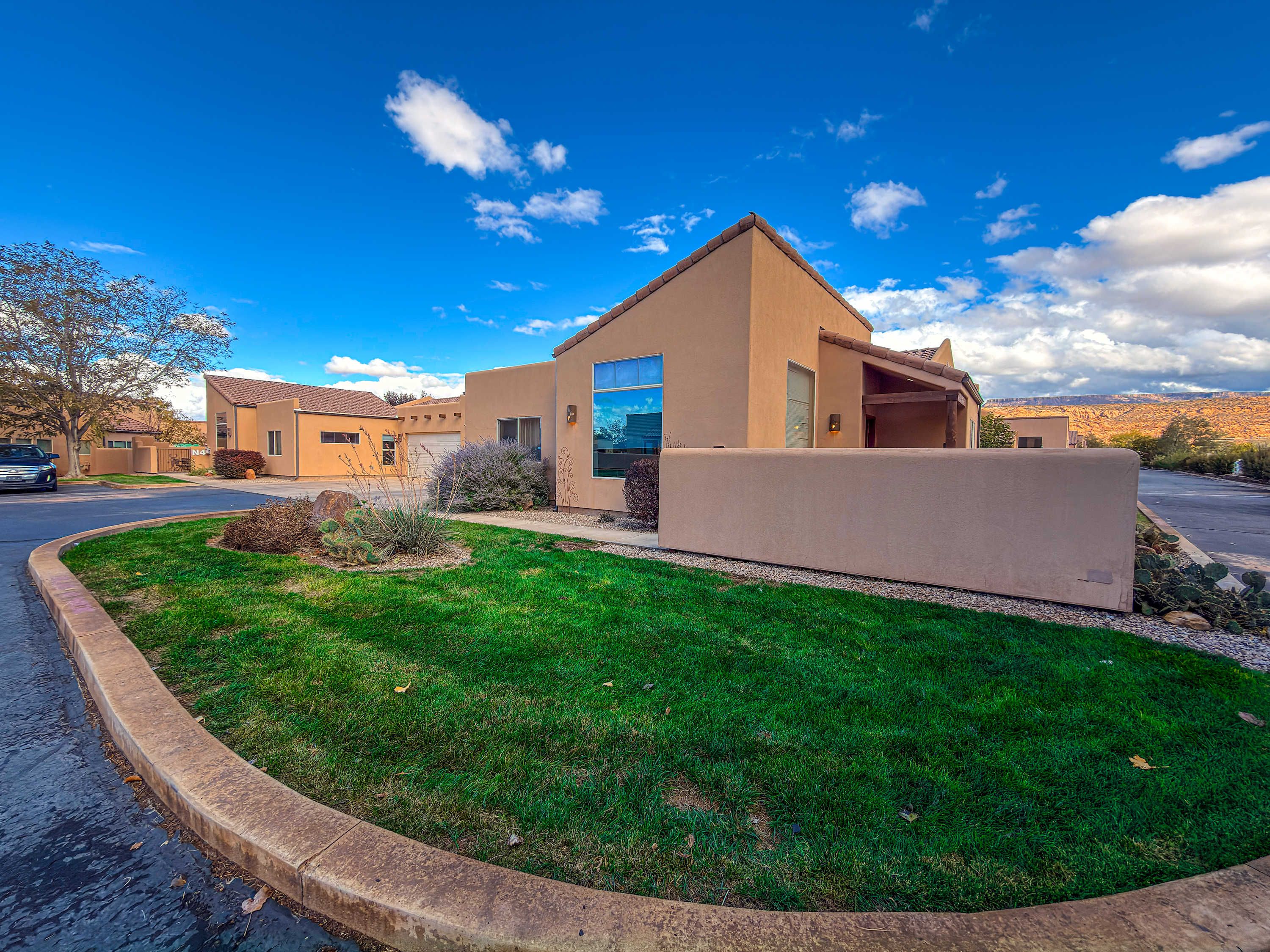 A modern two-story house with a flat roof, a well-maintained lawn, and a clear blue sky.