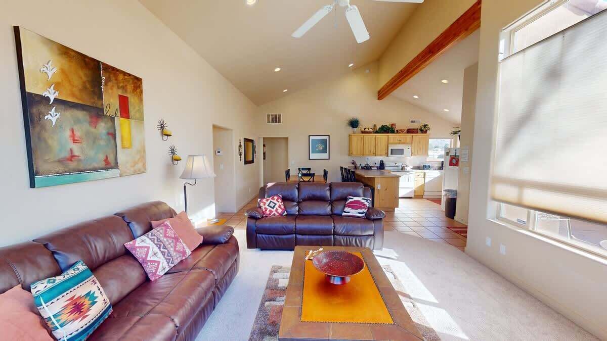 A spacious living room with a brown leather sofa, a coffee table, and a ceiling fan.
