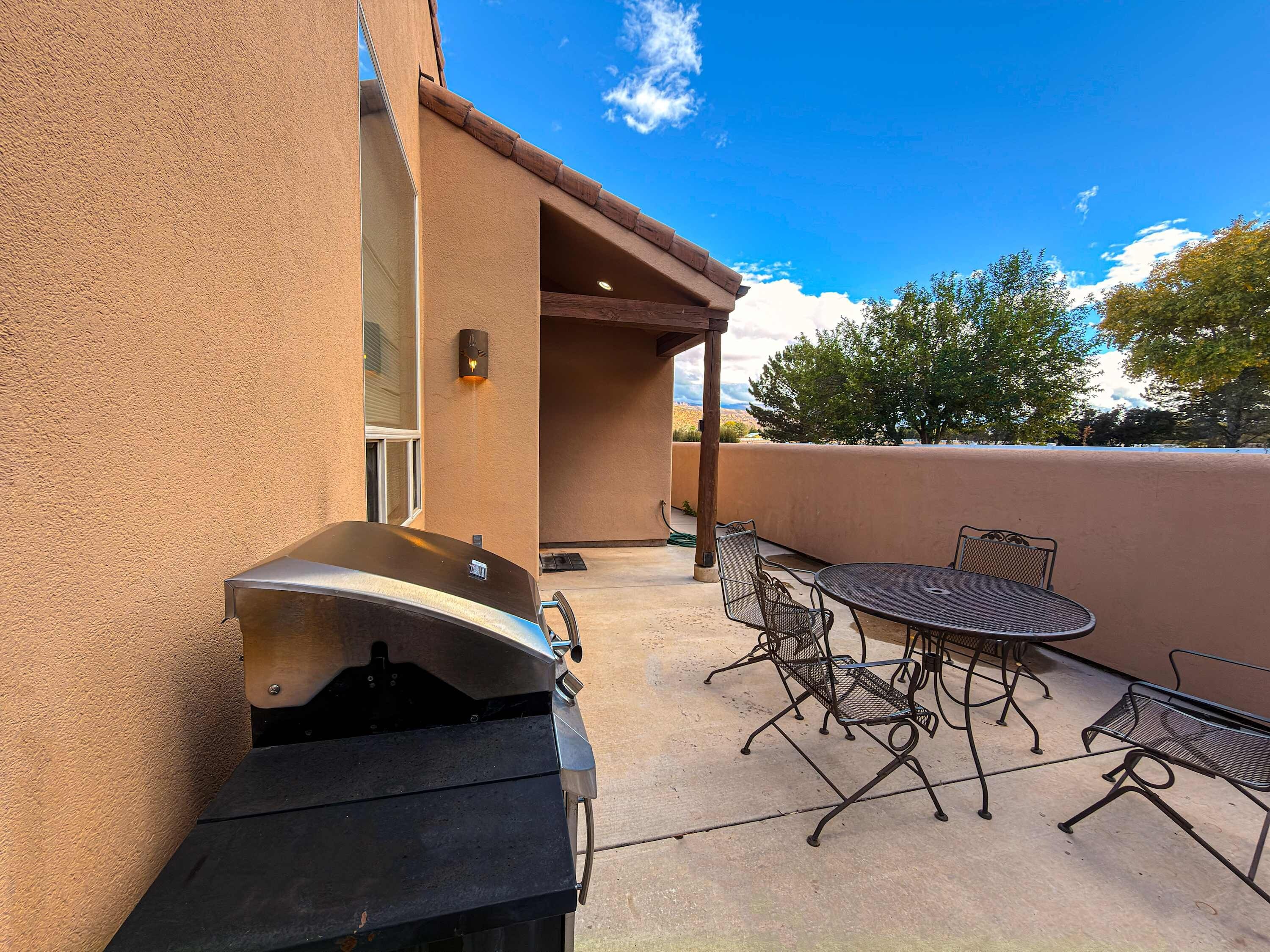 An outdoor patio with a barbecue grill, metal chairs, and a table.