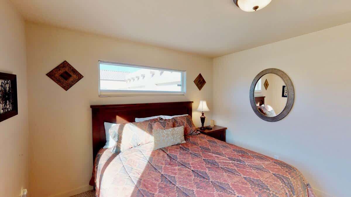 Een slaapkamer met een bed, nachtkastje, lamp, raam en spiegel.