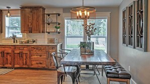 A kitchen with wooden cabinets, a large dining table, and a hanging light fixture. - Rustic Chic Home: 10 Mi to Otter Creek State Park! (Kingston)