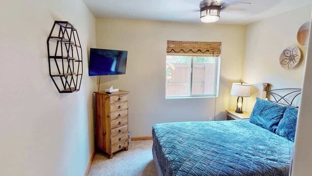 A bedroom with a bed, a dresser, a television, a window with a view, and a ceiling fan. - Arches East - 389, Downtown Moab 3-Bedroom Townhom (Moab)