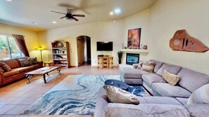 A living room with a sofa, a coffee table, a bookshelf, a flat-screen TV, and a fireplace. - Arches East - 389, Downtown Moab 3-Bedroom Townhom (Moab)