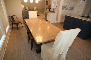 A dining area with a wooden table, chairs, and a kitchen in the background. - 5 Bedroom Beach Front Home with Screened in Deck (Cape San Blas)