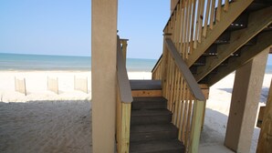 Un escalier en bois mène à une zone de plage d’où l’on a une vue dégagée sur l’océan.