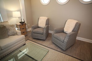 A living room with a sofa, two patterned armchairs, a glass coffee table, and a lamp.