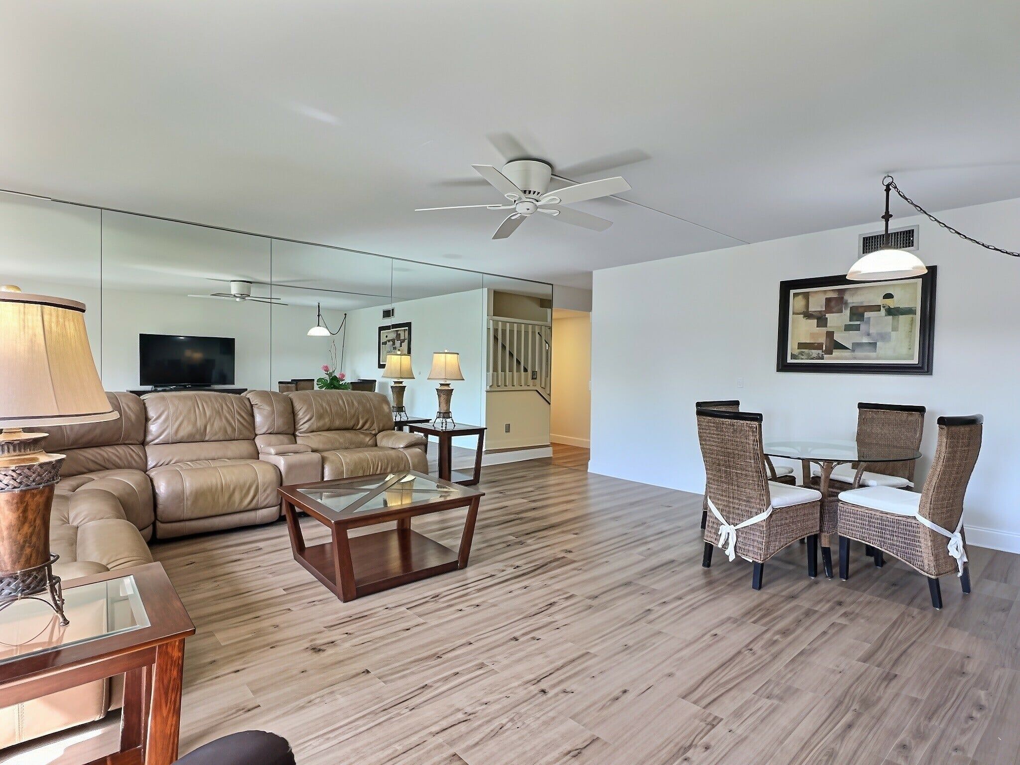A modern living room with a leather sofa, a glass coffee table, and a dining area with wicker chairs.