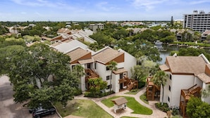 A residential area with modern houses, a central courtyard with a bench, and a body of water in the background. - Spacious vacation rental condo with lagoon views, beach access, and pool (Siesta Key)