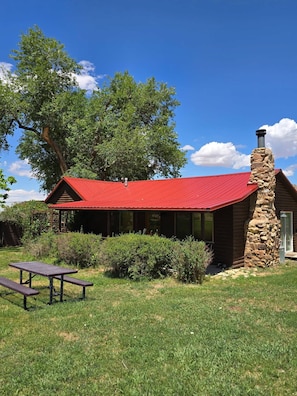A rustic cabin with a stone chimney, a red metal roof, and a picnic table in the foreground. - Pack Creek - Farm House! Phenomenal Location (Moab)