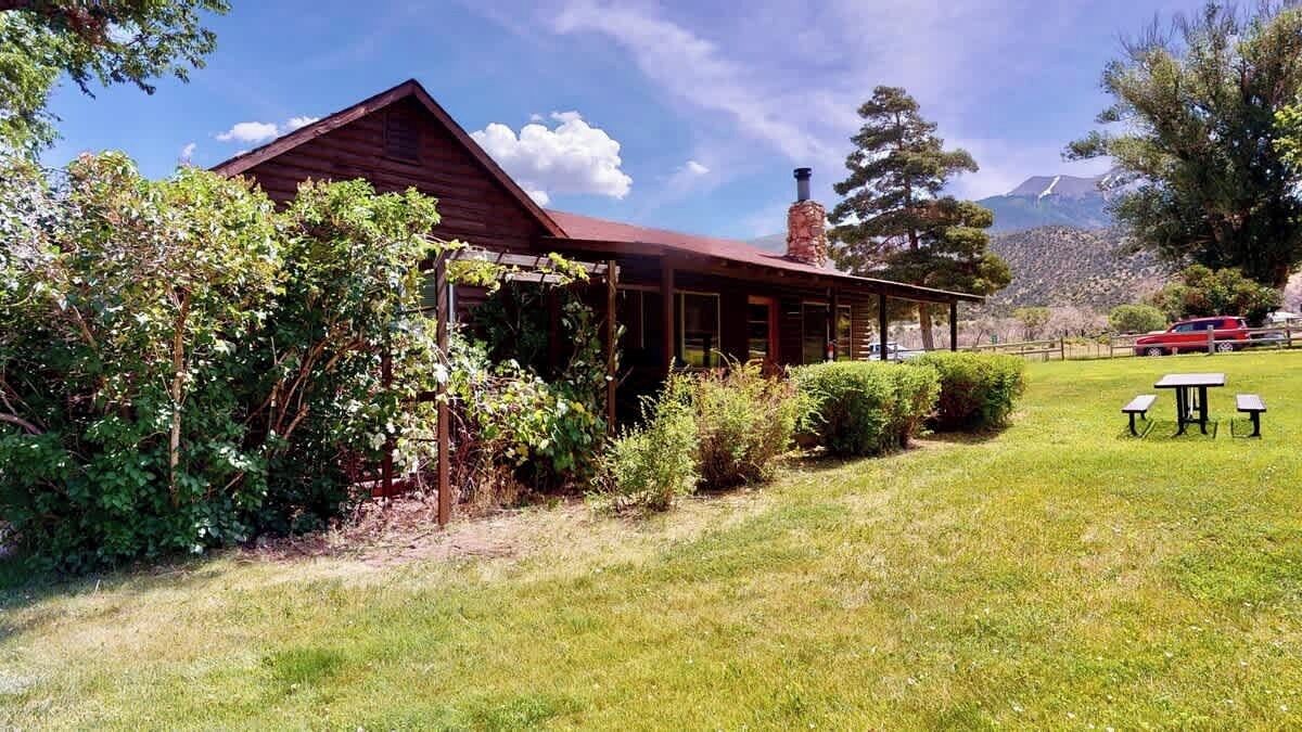 Une cabane en bois dotée d’un porche abrité, entourée d’une végétation luxuriante et avec une chaîne de montagnes en toile de fond.