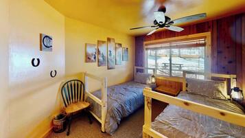 A room with bunk beds, a ceiling fan, a window with a view, and artwork on the wall.