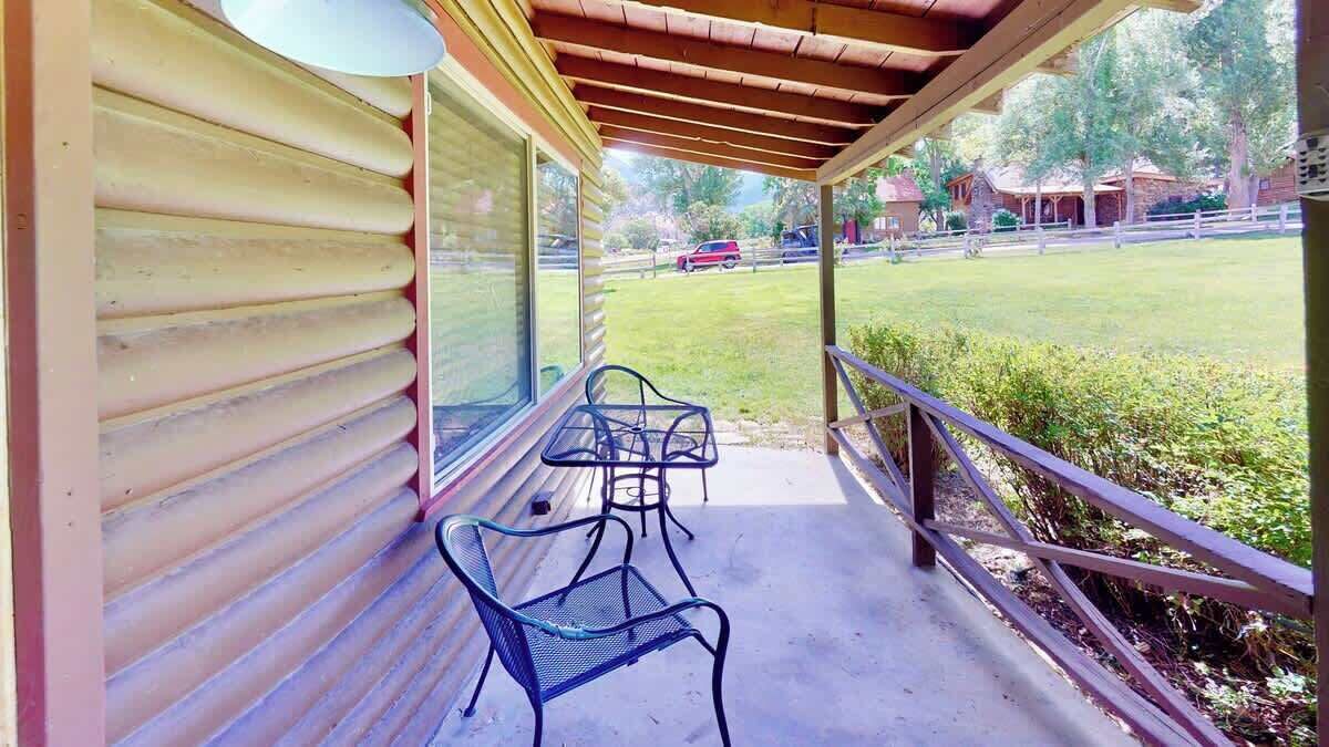 A covered porch with a view of a grassy area and a building in the background.