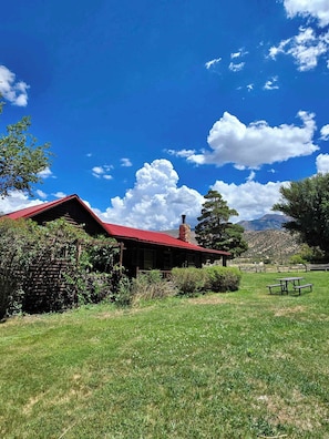 A rustic cabin with a red roof, surrounded by lush greenery and a clear blue sky. - Pack Creek - Farm House! Phenomenal Location (Moab)