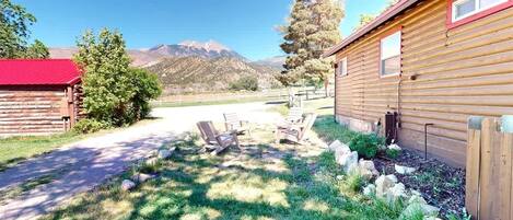 A wooden cabin with a red roof, a paved driveway, and a grassy area with outdoor seating.