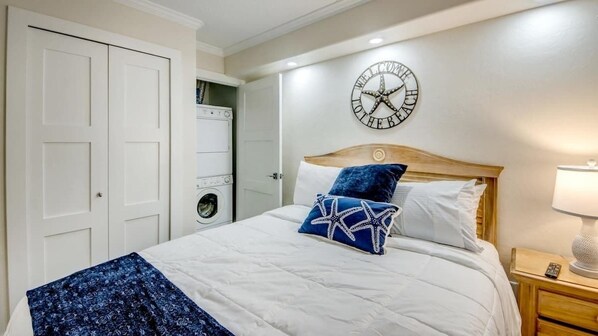 A bedroom with a bed, a clock, a washing machine, and a nightstand.