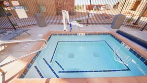 Une piscine avec un bord carrelé, une échelle de sécurité et une clôture.