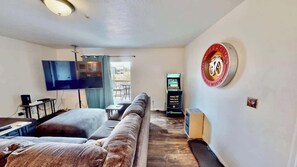 A living room with a sofa, a flat-screen TV, and a wall-mounted bike emblem. - Red Cliffs Condos - 1H, Enjoy Moab Rim Views While (Moab)
