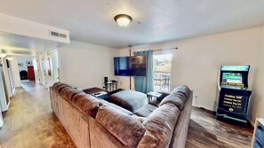 A living room with a sectional sofa, a flat-screen TV, and a gaming console. - Red Cliffs Condos - 1H, Enjoy Moab Rim Views While (Moab)