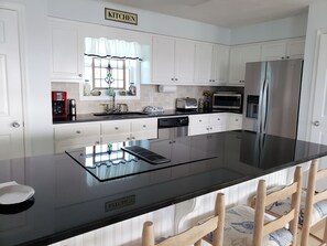 A modern kitchen with white cabinets, a stainless steel refrigerator, a built-in dishwasher, and a black countertop.