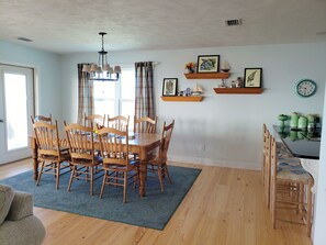 A dining area with a wooden table and chairs, a chandelier, and a window with curtains.