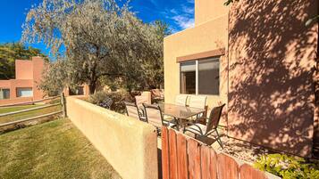 A patio area with a table and chairs, a wooden fence, and a tree.