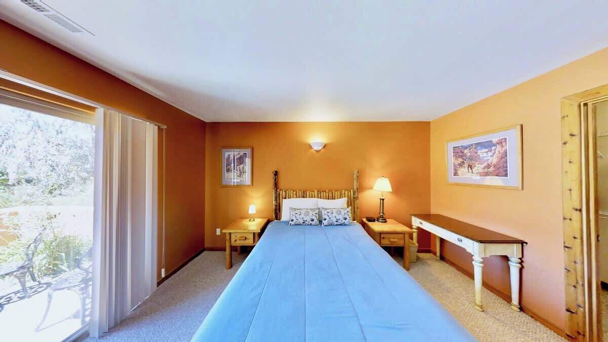 A hotel room with a bed, bedside tables, a desk, and a window with curtains.