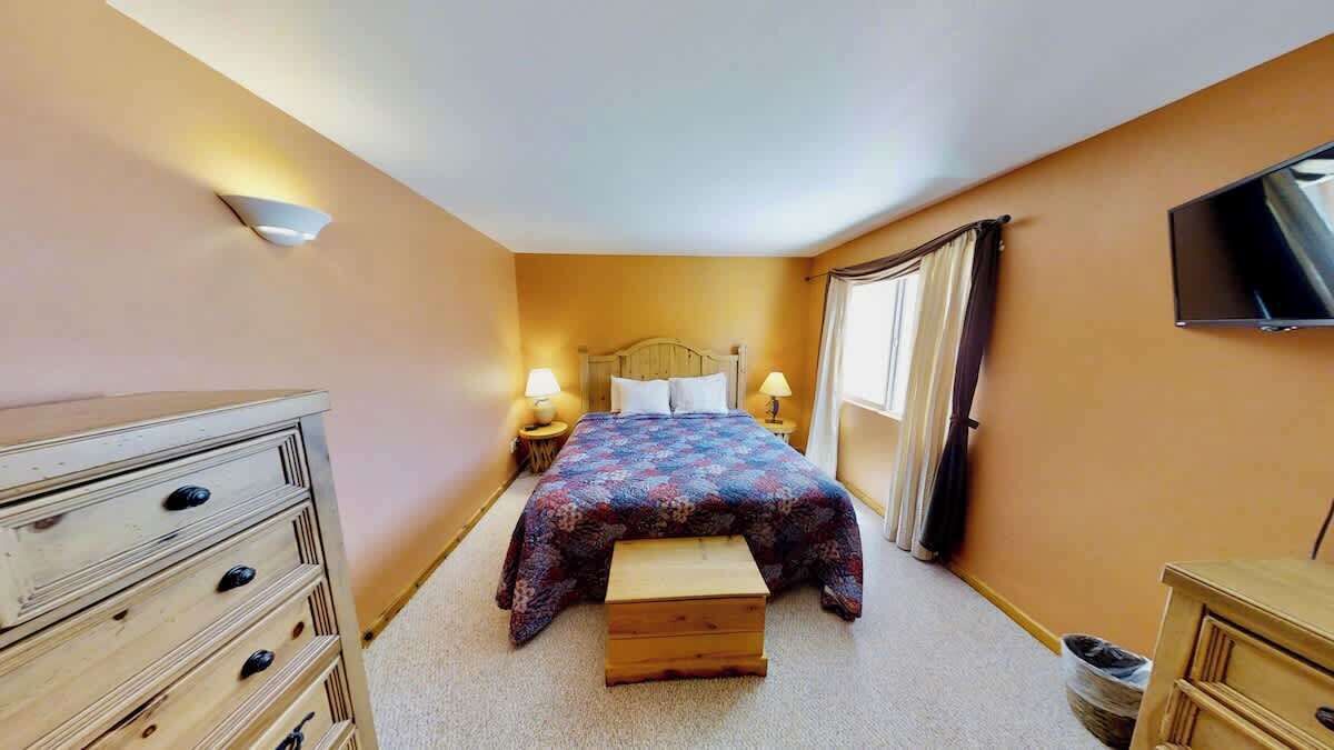 Une chambre à coucher avec un lit, des lampes de chevet, une commode, un téléviseur et une fenêtre avec des rideaux.