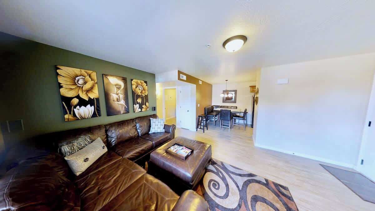 Un salon avec un canapé en cuir marron, une table basse et des œuvres d’art accrochées au mur. On aperçoit à l’arrière-plan un coin repas avec une table et des chaises.