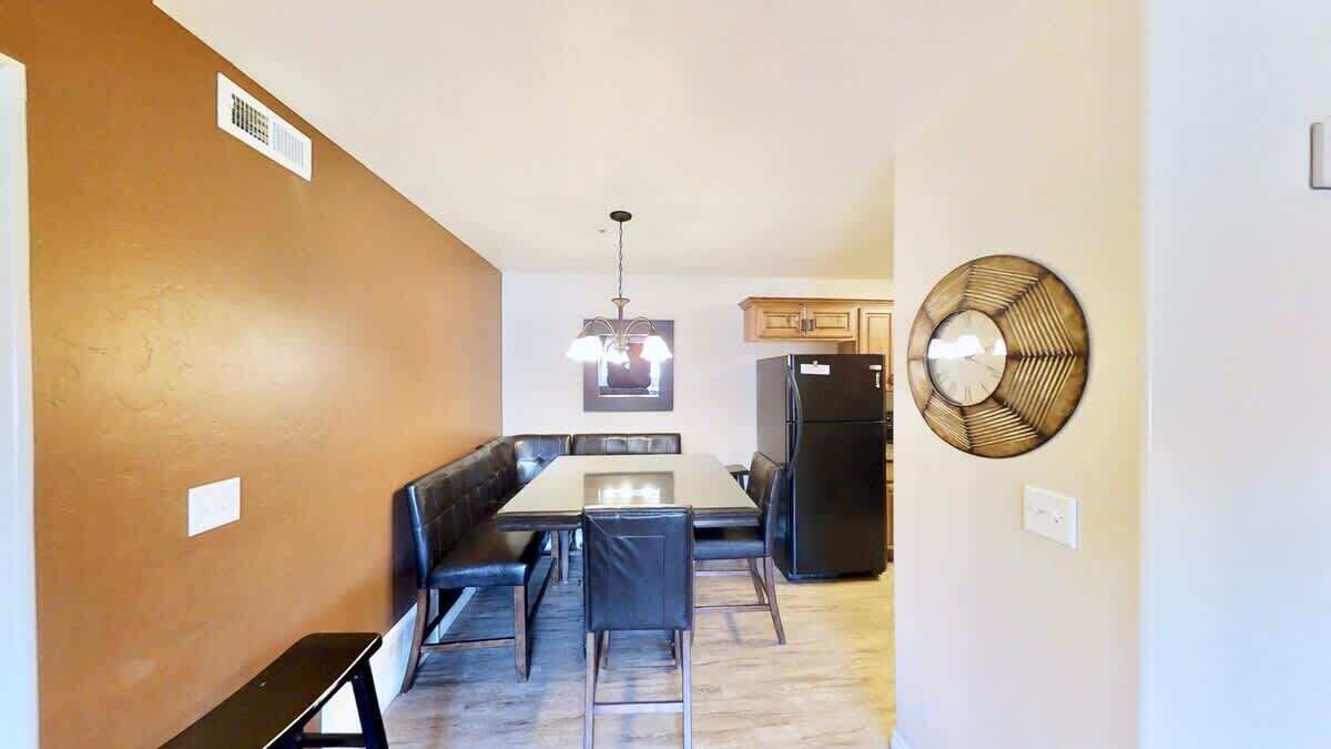 A dining area with a table and chairs, a refrigerator, and a wall-mounted fan.