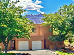 A two-story building with a garage, surrounded by trees and a mountain view. - Redesigned Red Rock condo with golf-course-view patio, fireplace, AC & pool (Moab)