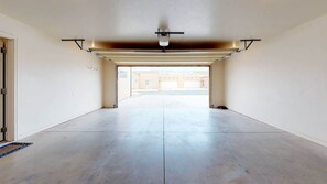 A spacious, empty garage with a concrete floor and a garage door at the far end. - Desert Oasis - X1, Private Hot Tub, Pet Friendly (Moab)