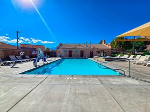 A clear blue pool with lounge chairs, a lifeguard stand, and a building with a tiled roof in the background. - Desert Oasis - X1, Private Hot Tub, Pet Friendly (Moab)