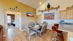 A dining area with a wooden table and chairs, a kitchen with wooden cabinets, and artwork on the walls.